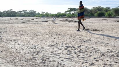 Mann in traditioneller Kleidung der Turkana Volksgruppe läuft über ein ausgetrocknetes Flussbett